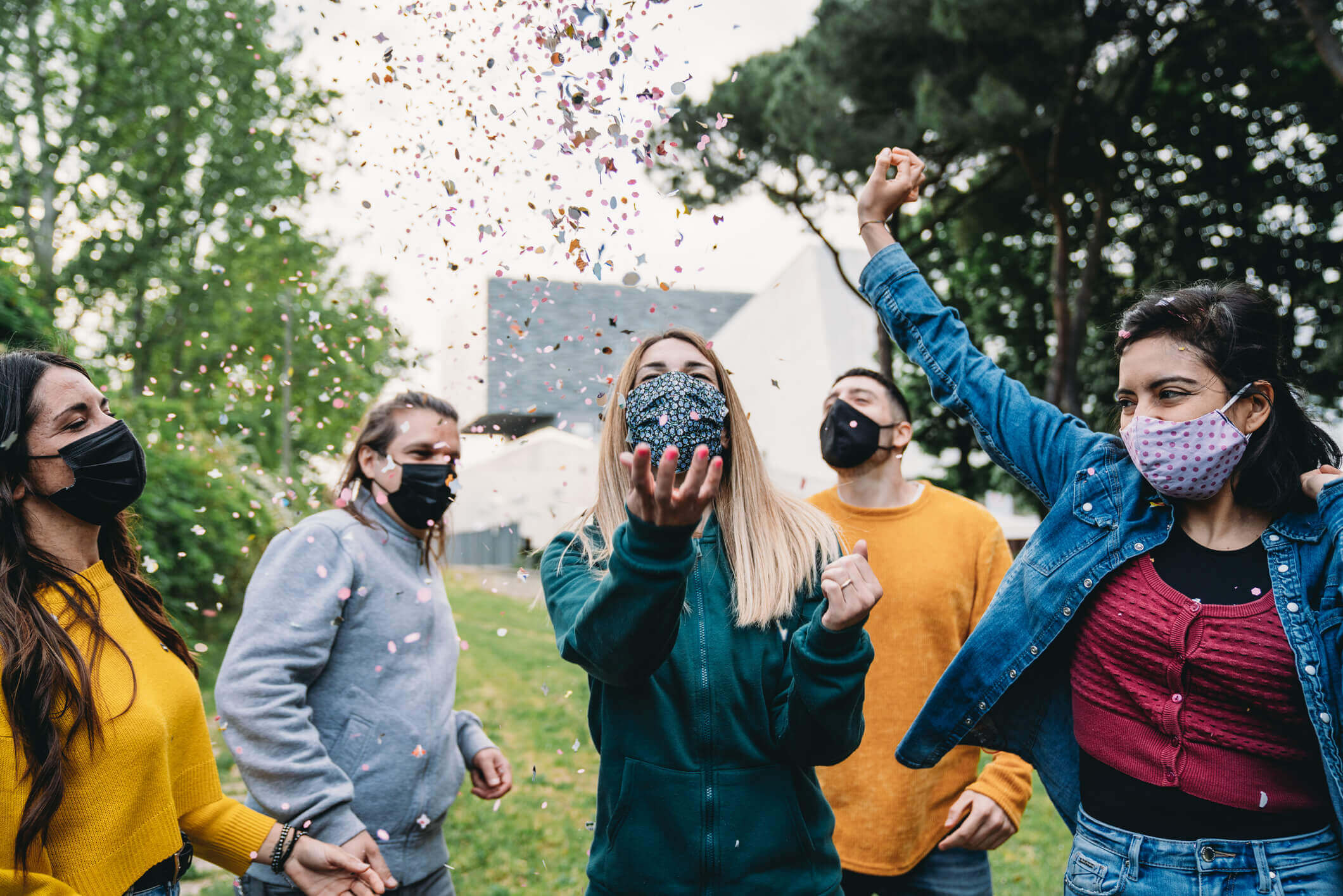 Group of friends celebrating with confetti while they are dancing outdoors