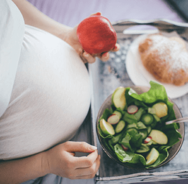 Pregnant woman sitting in front of a salad and holding an apple