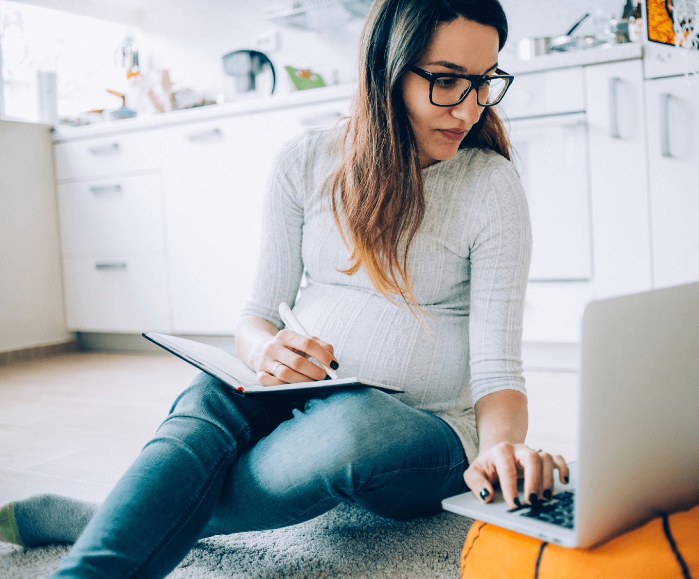 Woman with glasses writing notes while using a laptop