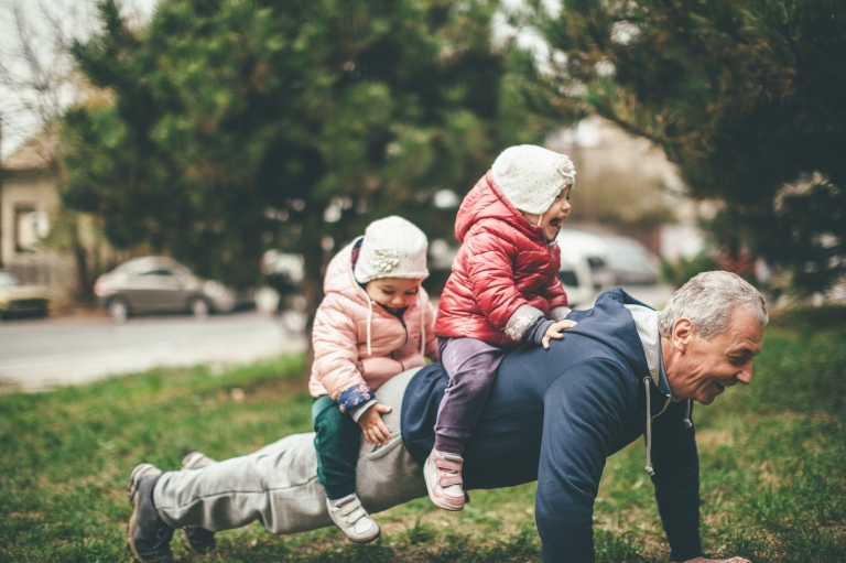 grandfather doing push-ups with kids on his back in the park